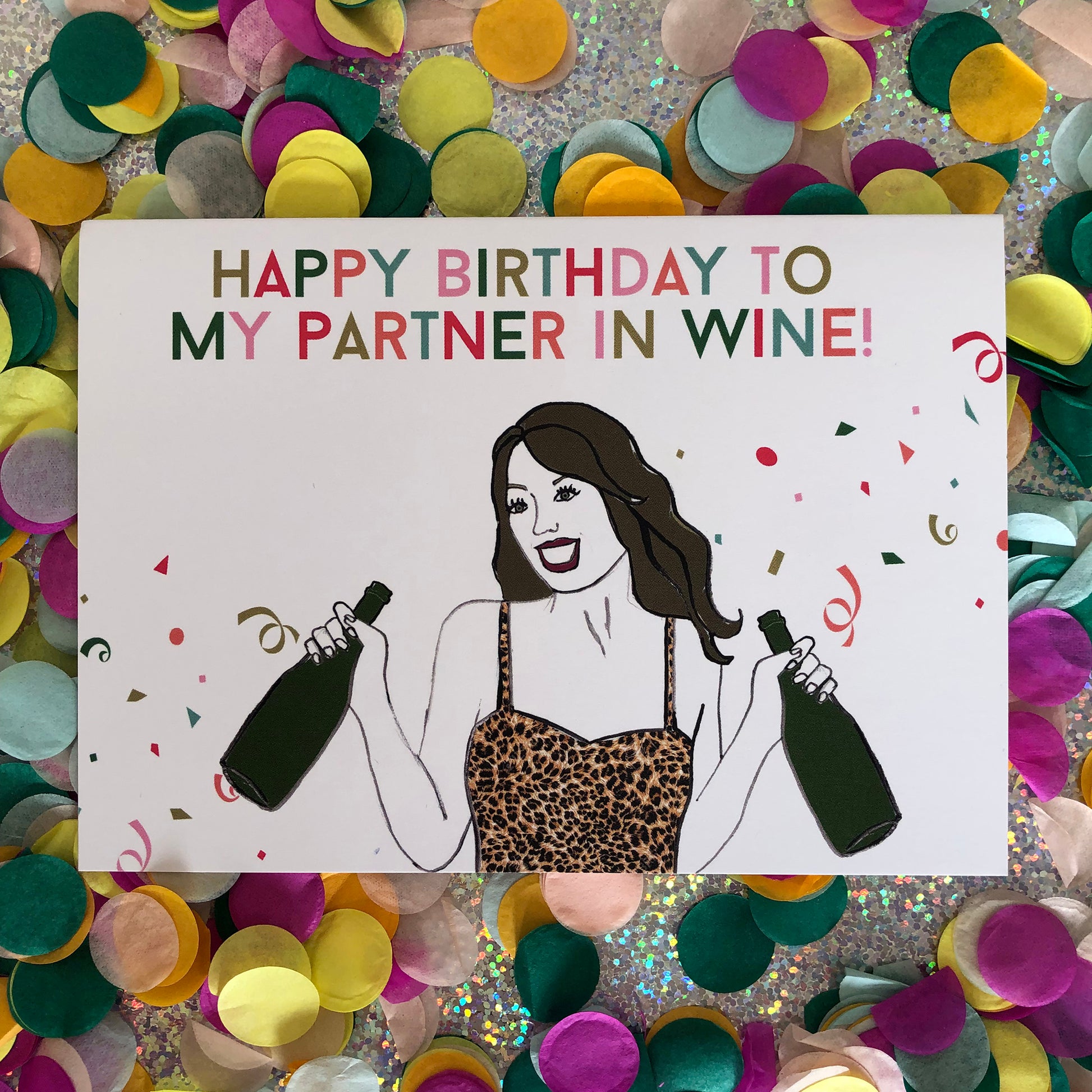 Image shows a fun and fabulous white birthday card with an illustration of a woman in a leopard print top holding 2 bottles of wine and the wording 'Happy Birthday to my partner in wine'..