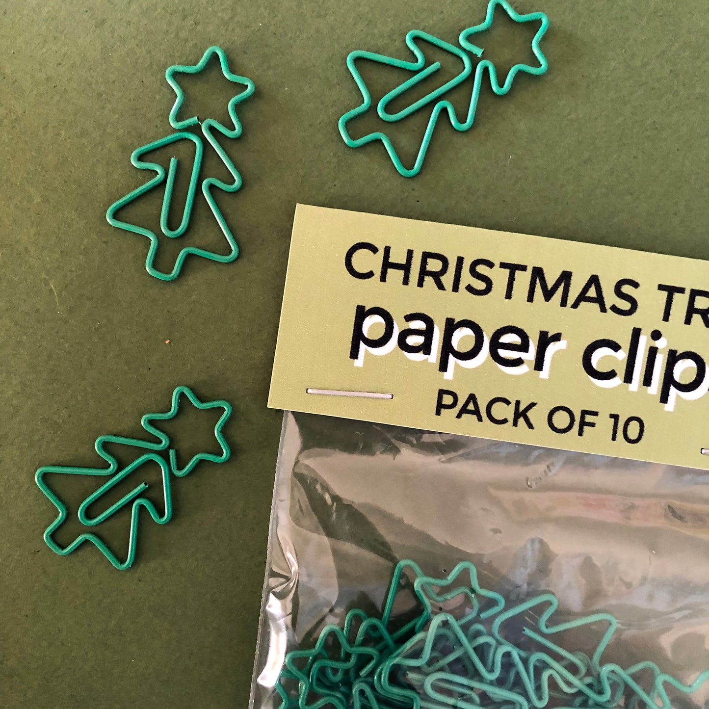 Image shows a collection of cute Christmas tree shaped paperclips on a green background.