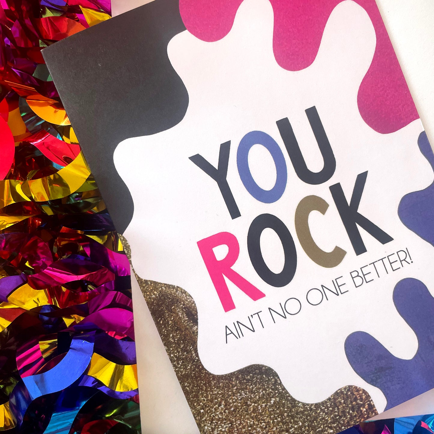 Image shows a bright greetings card with colourful, abstract shapes around the edge and the wording "You Rock ain't no one better"