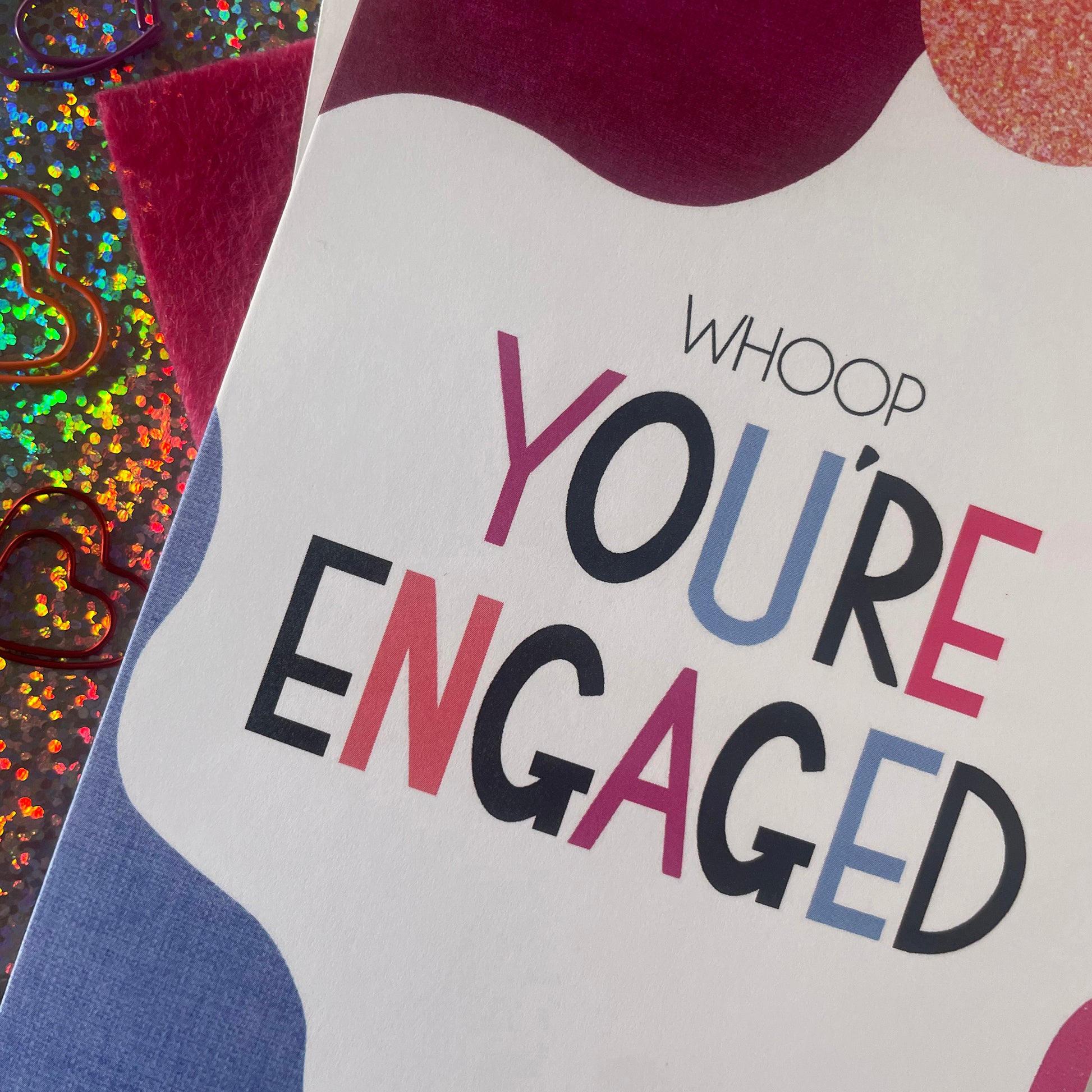 Image shows a bright greetings card with colourful, abstract shapes around the edge and the wording "Whoop you're engaged""