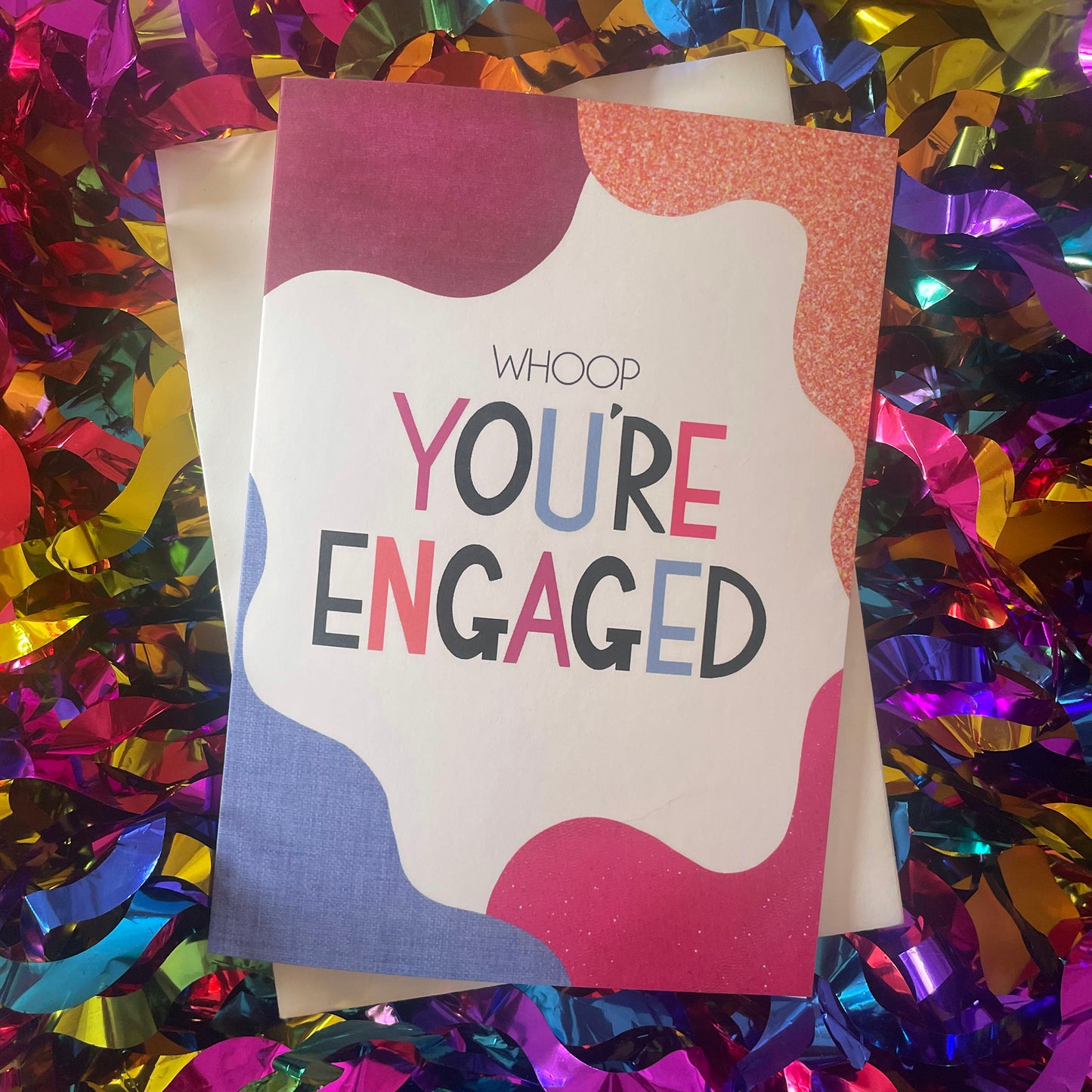Image shows a bright greetings card with colourful, abstract shapes around the edge and the wording "Whoop you're engaged""
