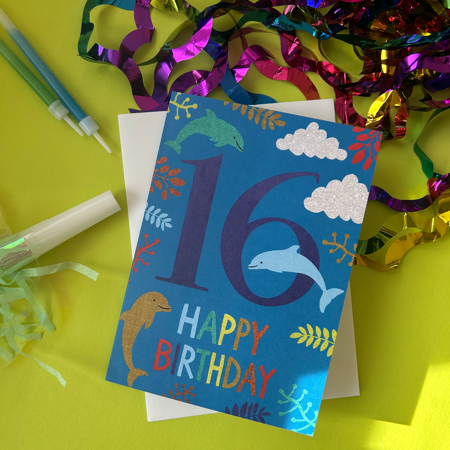 Birthday card with number 16 and dolphins on a yellow background with party supplies.
