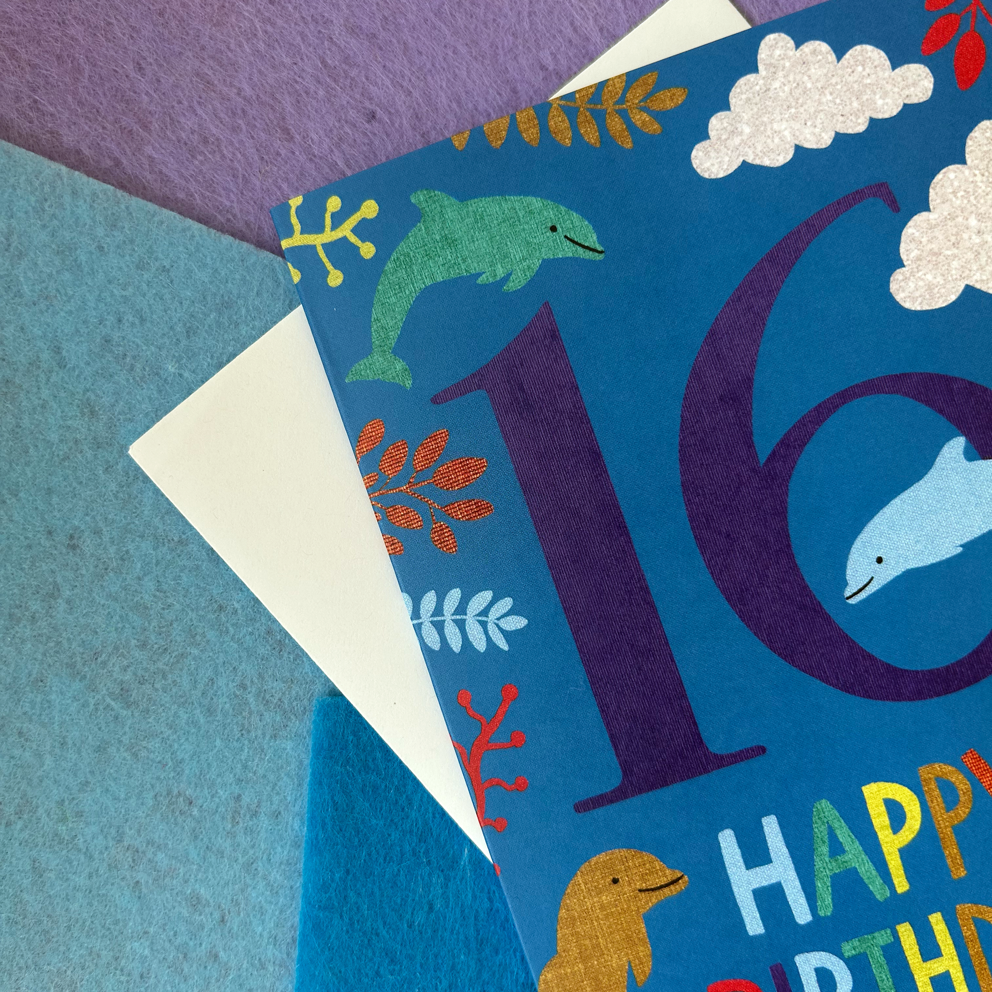 Birthday card with number 16 and sea-themed illustrations on a textured surface.