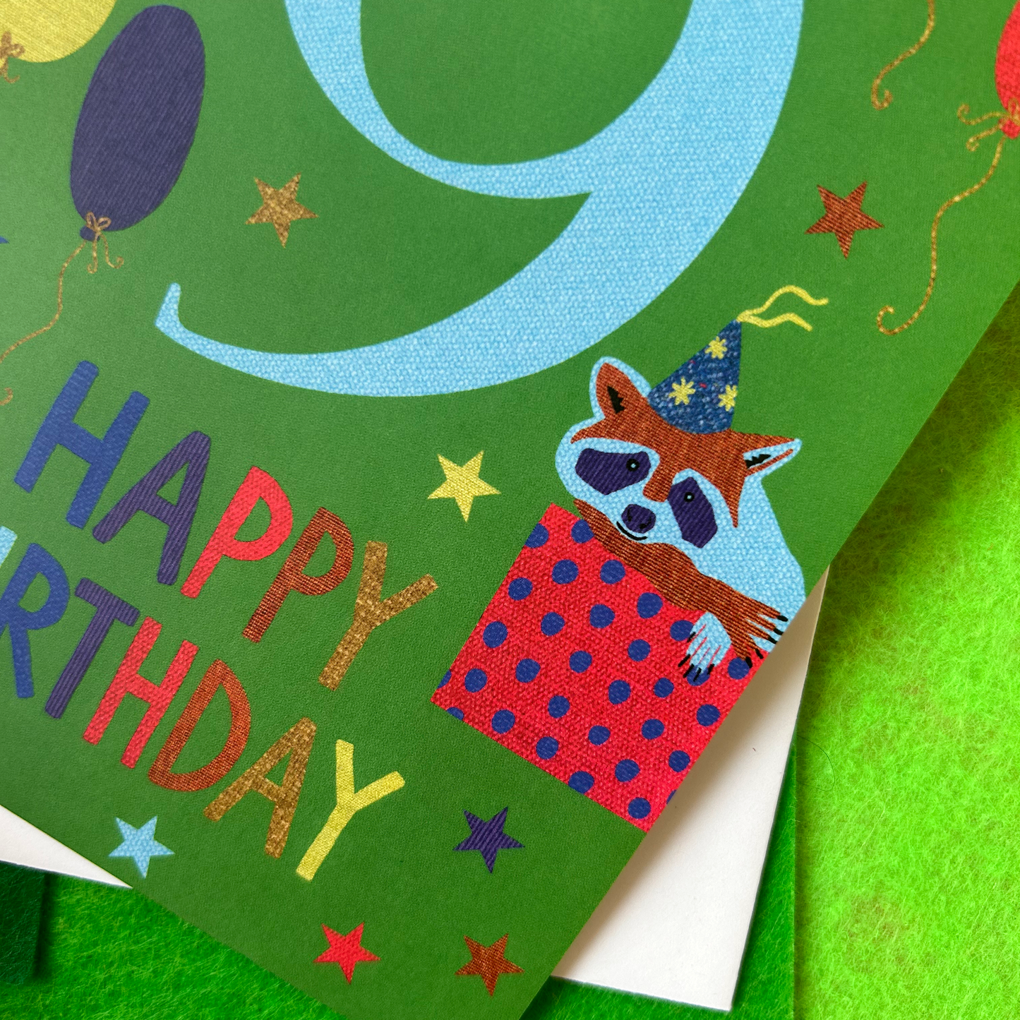 Children's birthday card with a raccoon illustration and colorful text on a green background