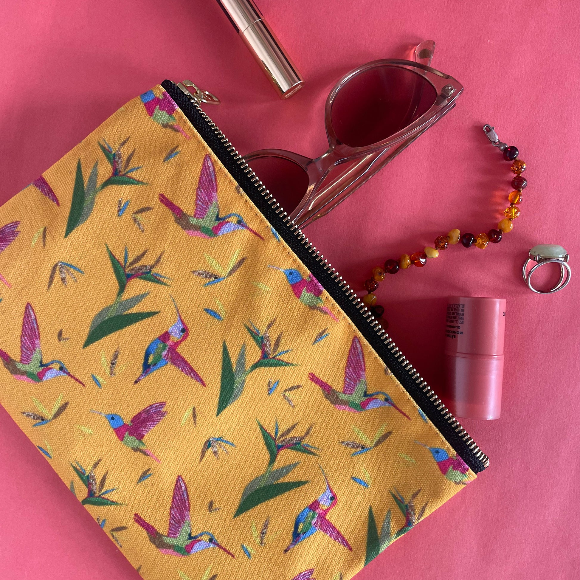 Image shows a bright yellow zip pouch with a colourful hummingbird and bird of paradise plant print.