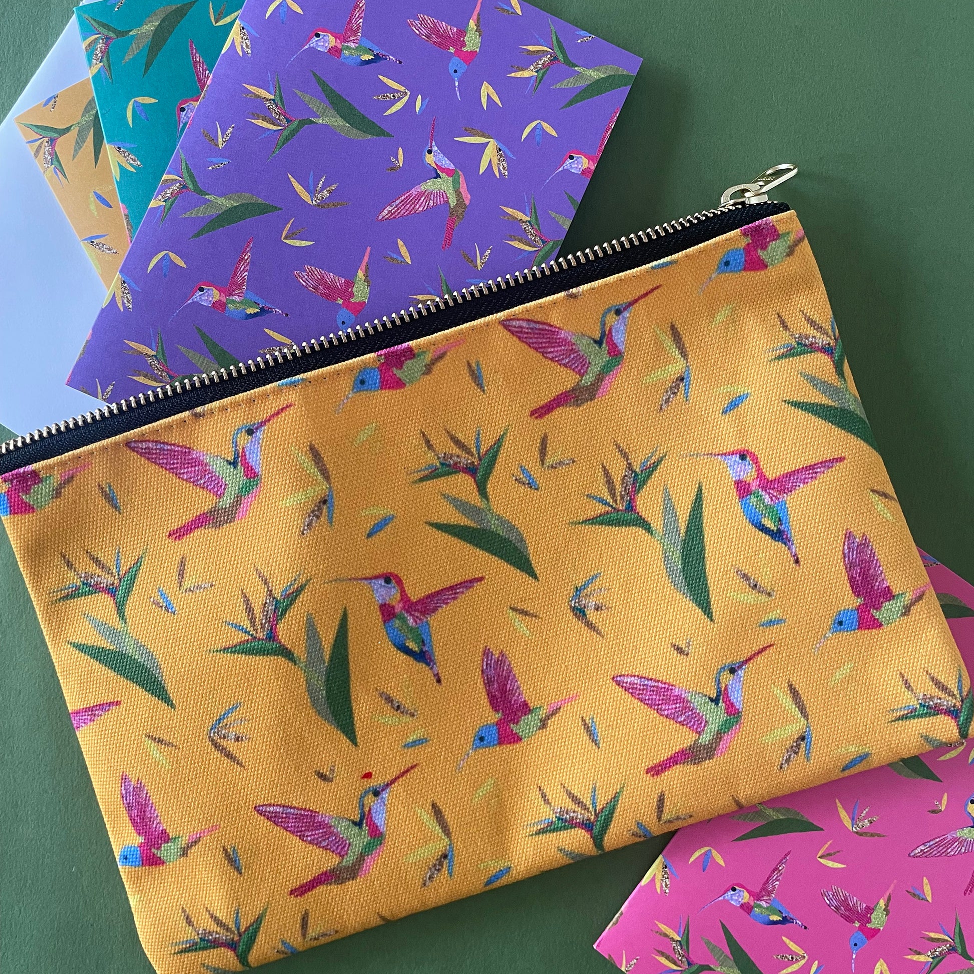 Image shows a bright yellow zip pouch with a colourful hummingbird and bird of paradise plant print.