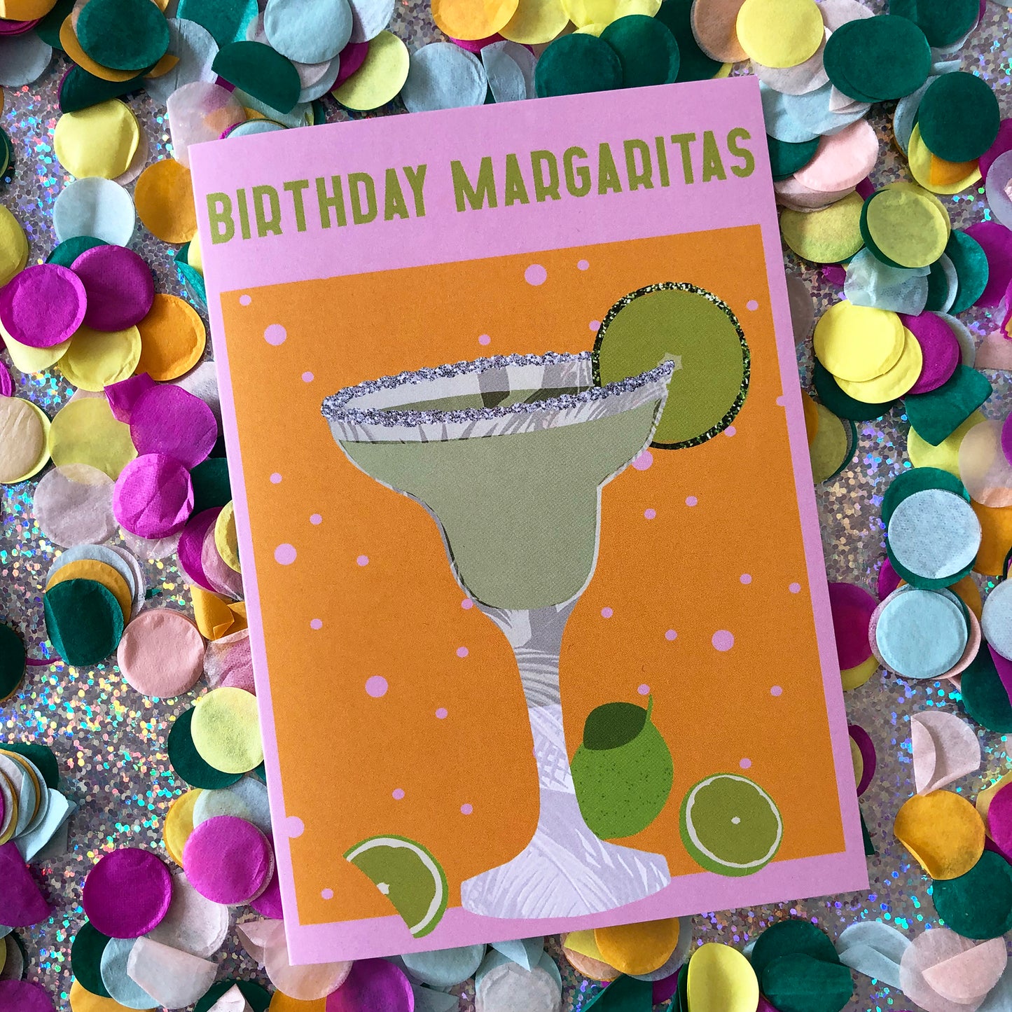 Image shows a yellow and pink coloured  birthday card with the greeting 'Birthday Margaritas' and a lime green cocktail with limes and a glitter salt rim.