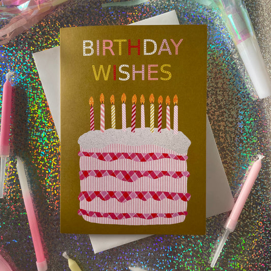 Image shows an ochre coloured  birthday card with the greeting 'Birthday Wishes' and a pink and white collaged cake with candles/ 