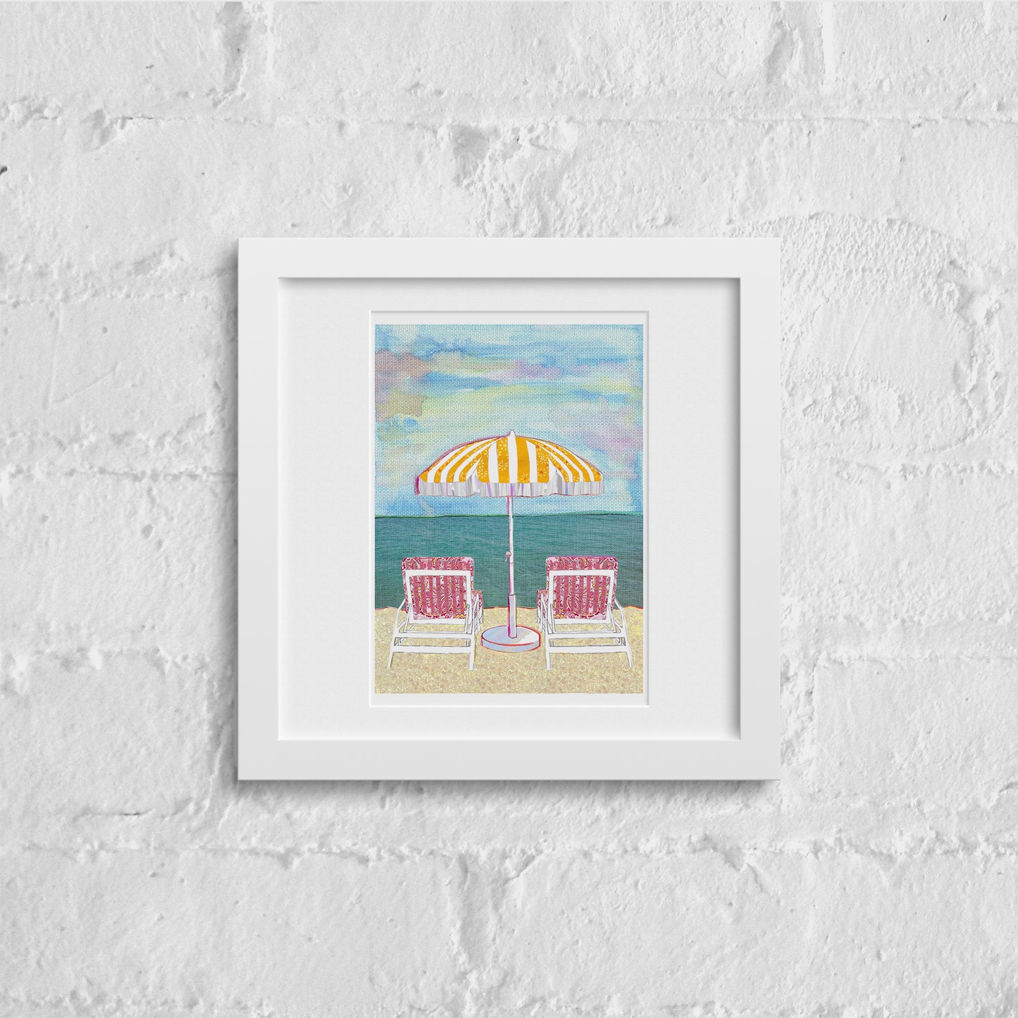 White wall with a white framed illustration of a pretty pastel beach scene featuring 2 chairs and a parasol by the sea