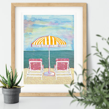 Framed image of a pretty pastel beach scene featuring 2 chairs and a parasol by the sea