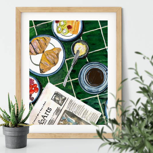 Framed artwork of a breakfast scene with croissants, coffee, and a newspaper on a green tiled table.