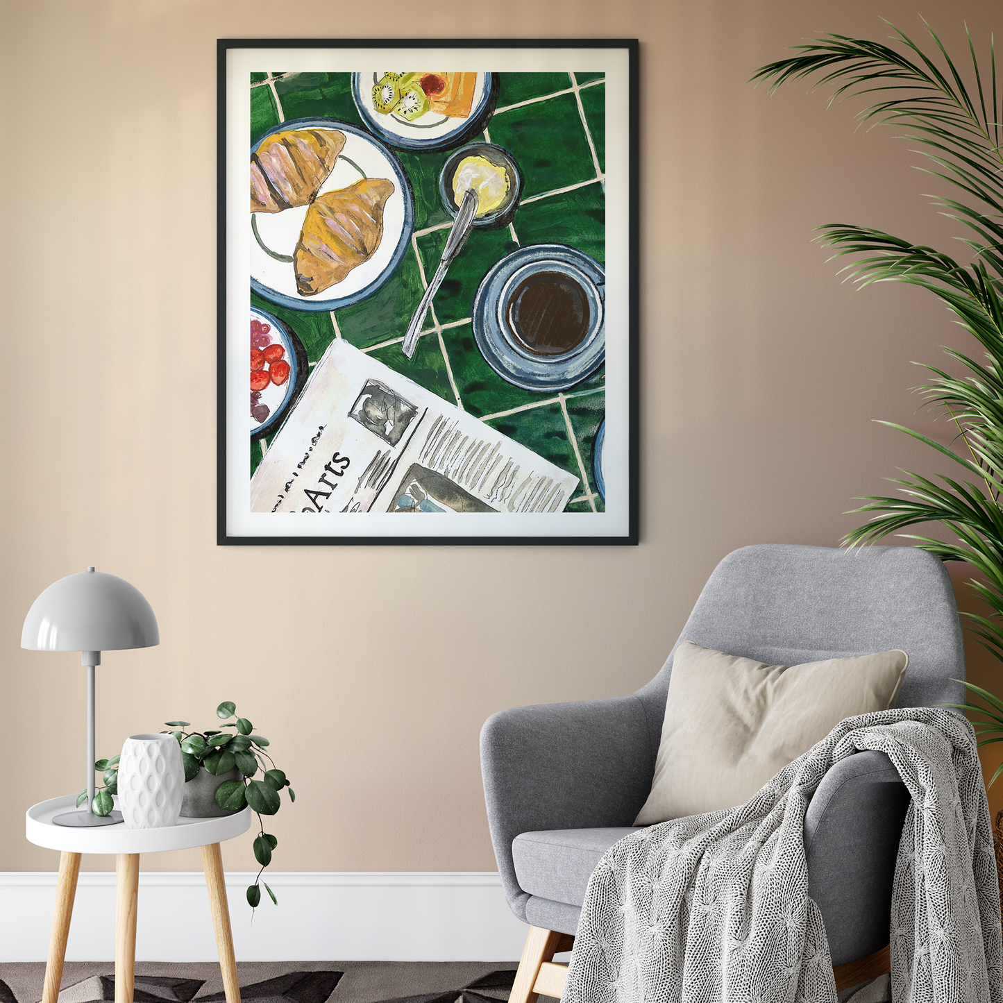 Framed artwork of a breakfast scene on a wall above a gray armchair.