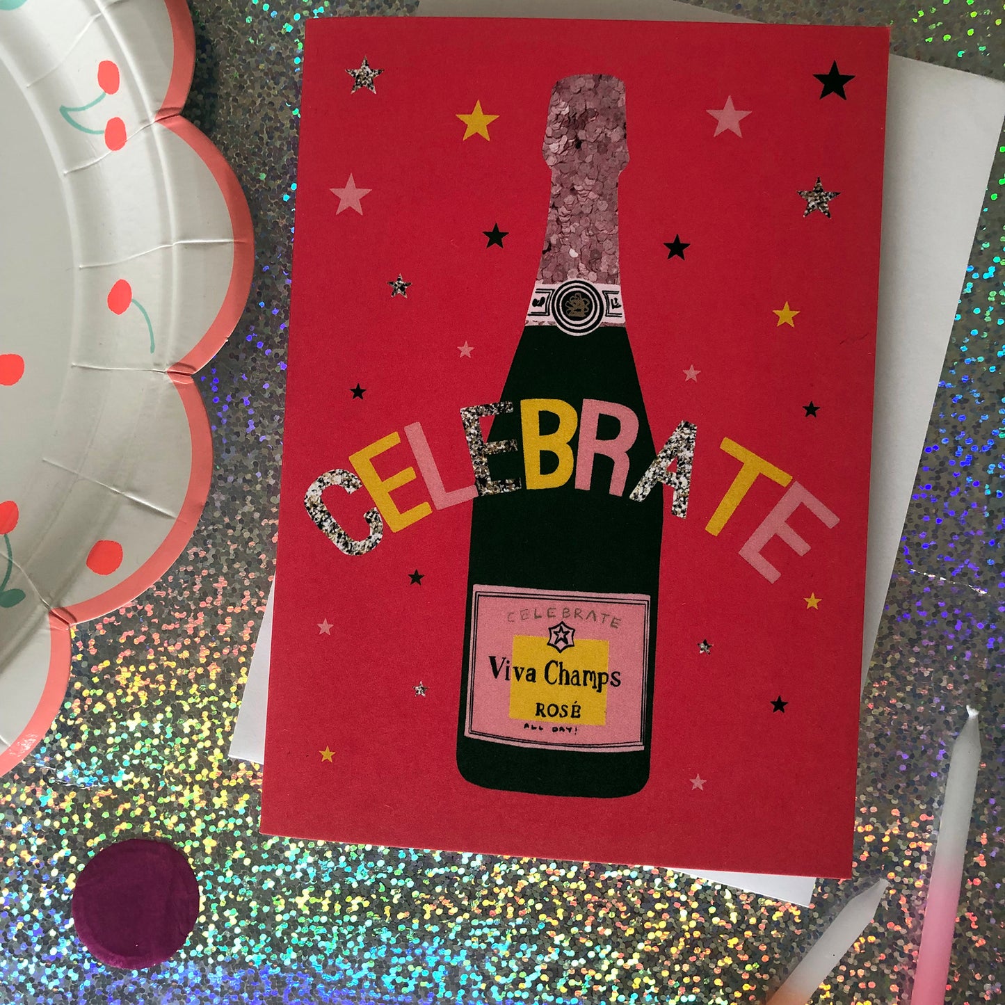 Image shows a bright red celebration card featuring a champagne bottle and stars