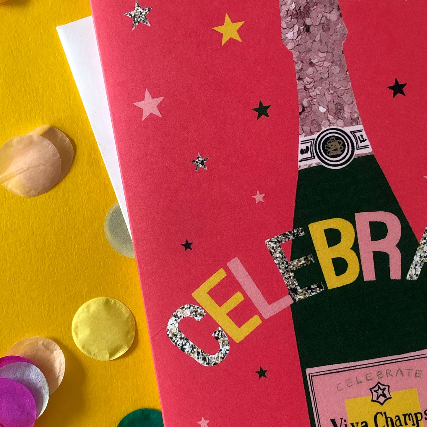 Image shows a bright red celebration card featuring a champagne bottle and stars