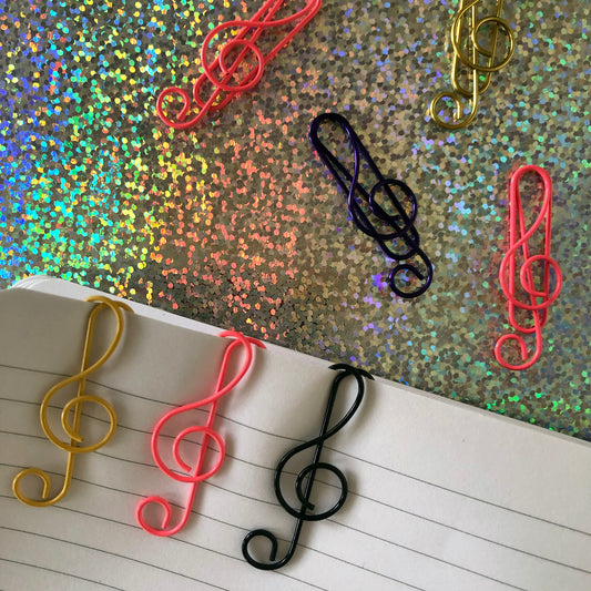 Image shows a set of pink, black and gold, treble clef shaped paperclips.