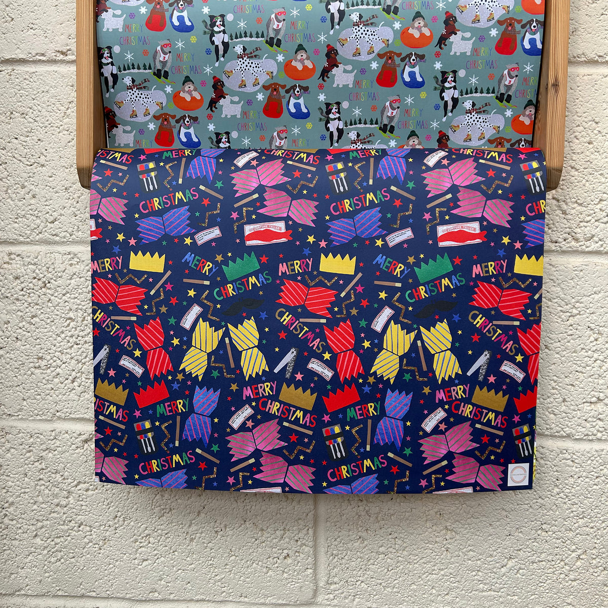 Christmas-themed patterned wrapping paper with bright, colourful Christmas Cracker design on a wooden rack.