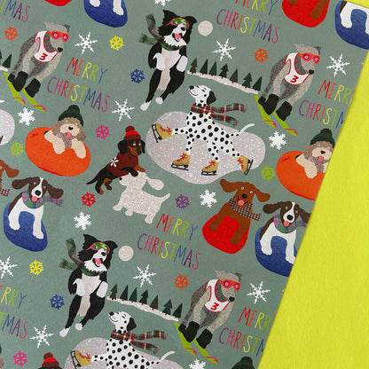 A close-up of a Christmas-themed dog print fabric or wrapping paper featuring illustrated dogs in winter activities on a muted sage green background.