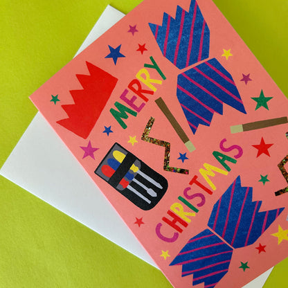 A peach Christmas card with colourful illustrated crackers, stars, and the words “MERRY CHRISTMAS,” placed on top of a white envelope against a bright yellow-green background.