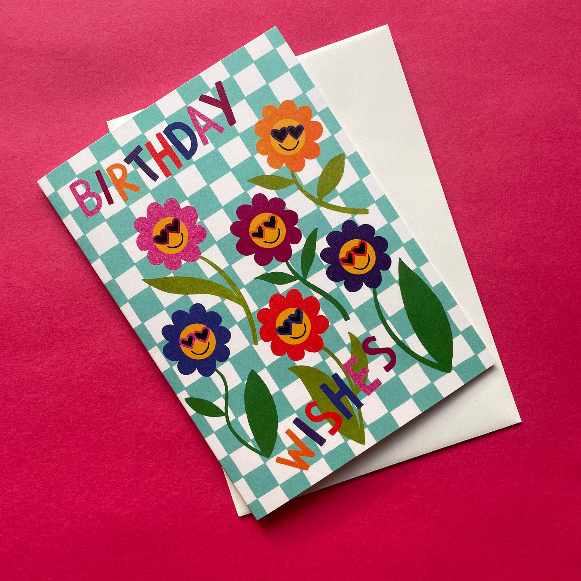 Birthday card with colorful flowers and 'Happy Birthday' text on a checkered background, with a white envelope.