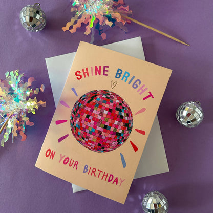 Birthday card with disco ball design and text 'Shine Bright on Your Birthday' on a purple background with disco balls.
