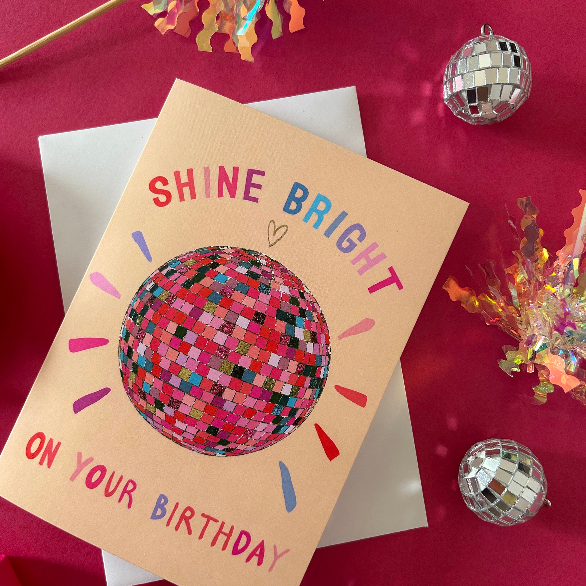 Birthday card with disco ball illustration and 'Shine Bright on Your Birthday' text on a red background.