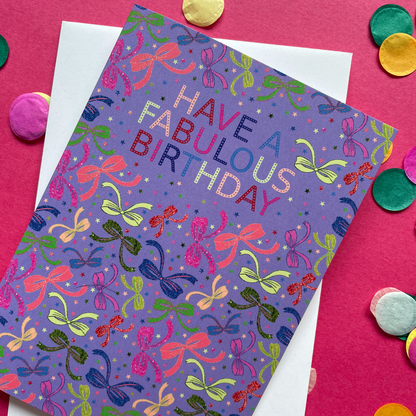 Image shows a lilac birthday card with neon and sparkly bow illustrations and a cloud with multicoloured wording that reads 'Have a fabulous birthday"
