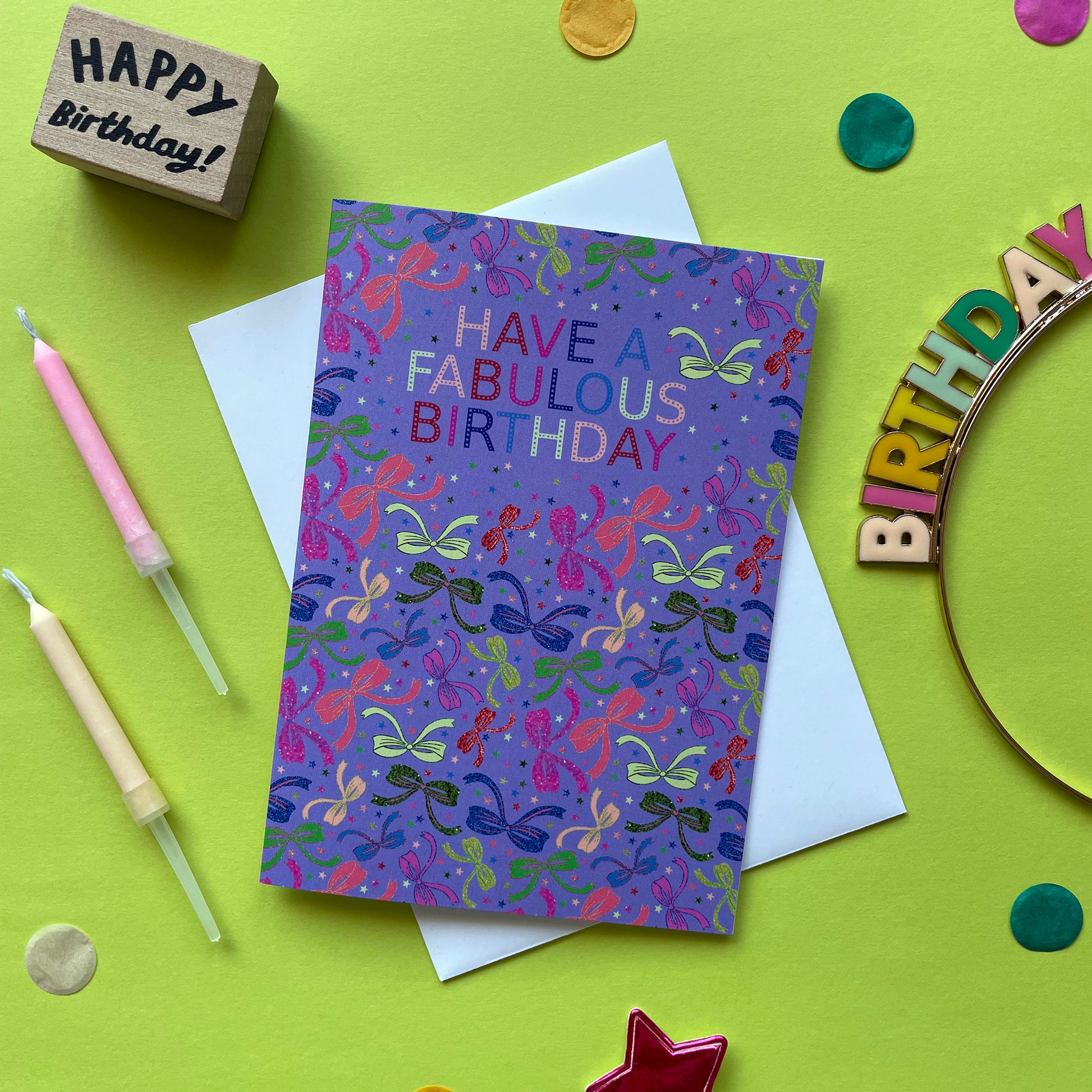Image shows a lilac birthday card with neon and sparkly bow illustrations and a cloud with multicoloured wording that reads 'Have a fabulous birthday"