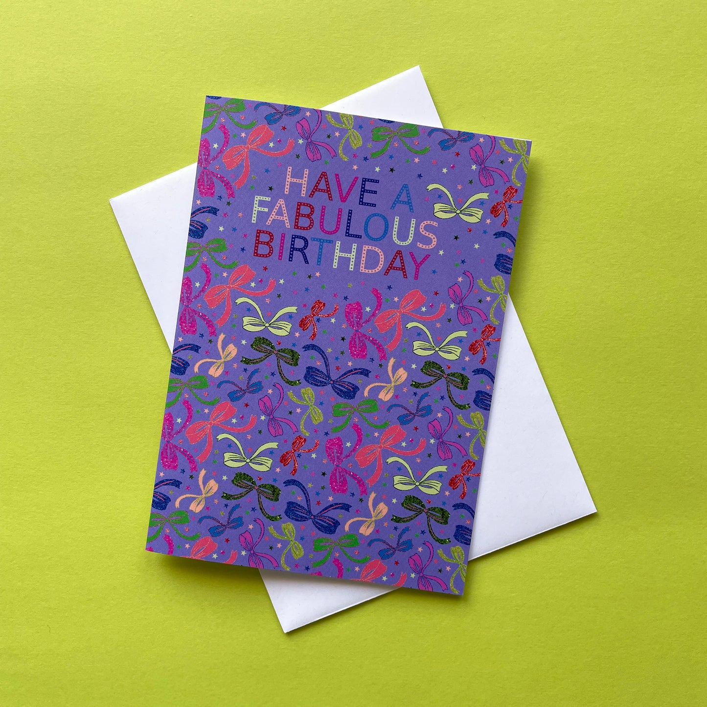 Image shows a lilac birthday card with neon and sparkly bow illustrations and a cloud with multicoloured wording that reads 'Have a fabulous birthday"