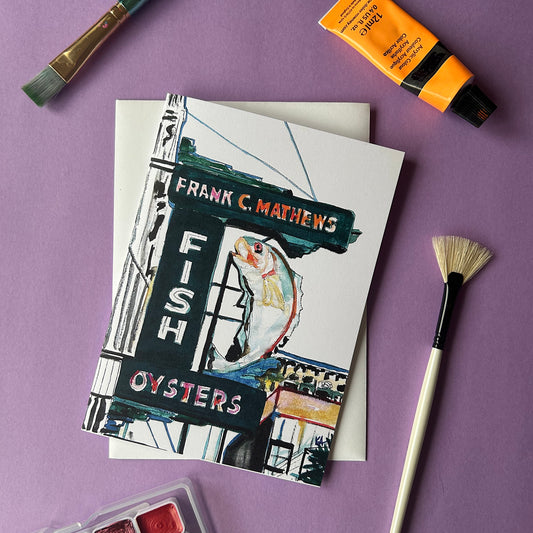 Card with a fish and oysters sign design on a purple background with art supplies.
