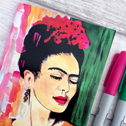 Image shows  a full colour notebook featuring a bright, hand painted illustration of Frida Kahlo