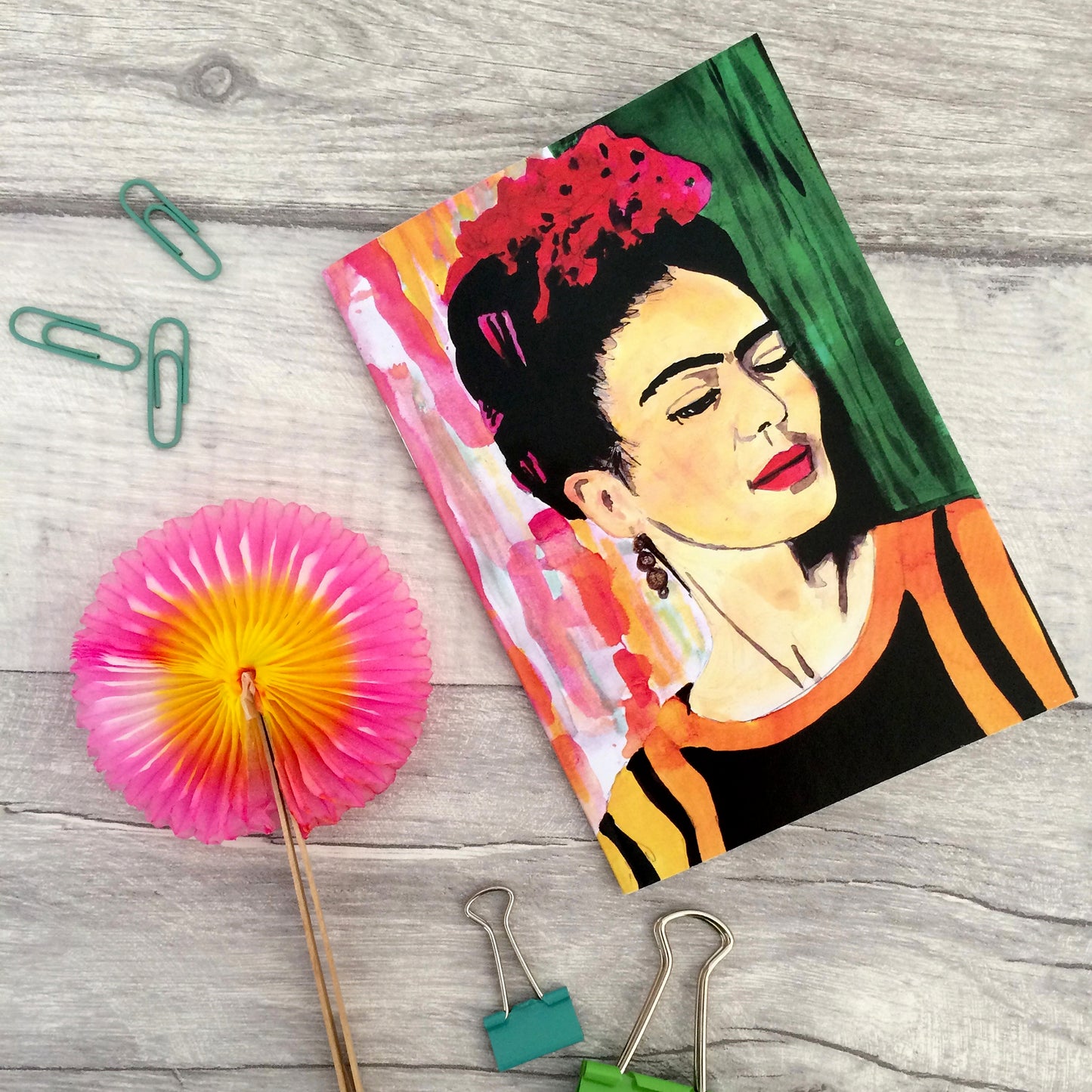 Image shows  a full colour notebook featuring a bright, hand painted illustration of Frida Kahlo