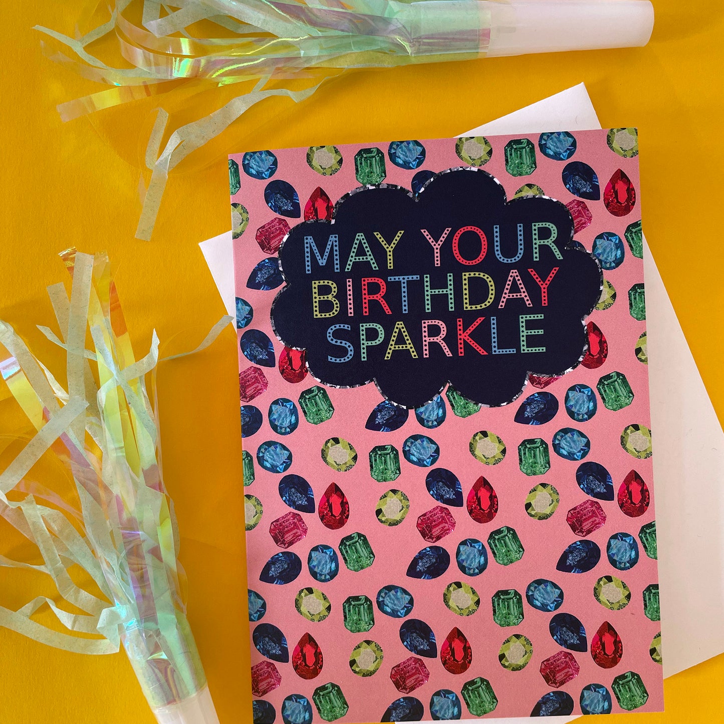 Image shows a sparkly gemstone patterned greetings card with the words may your birthday sparkle.