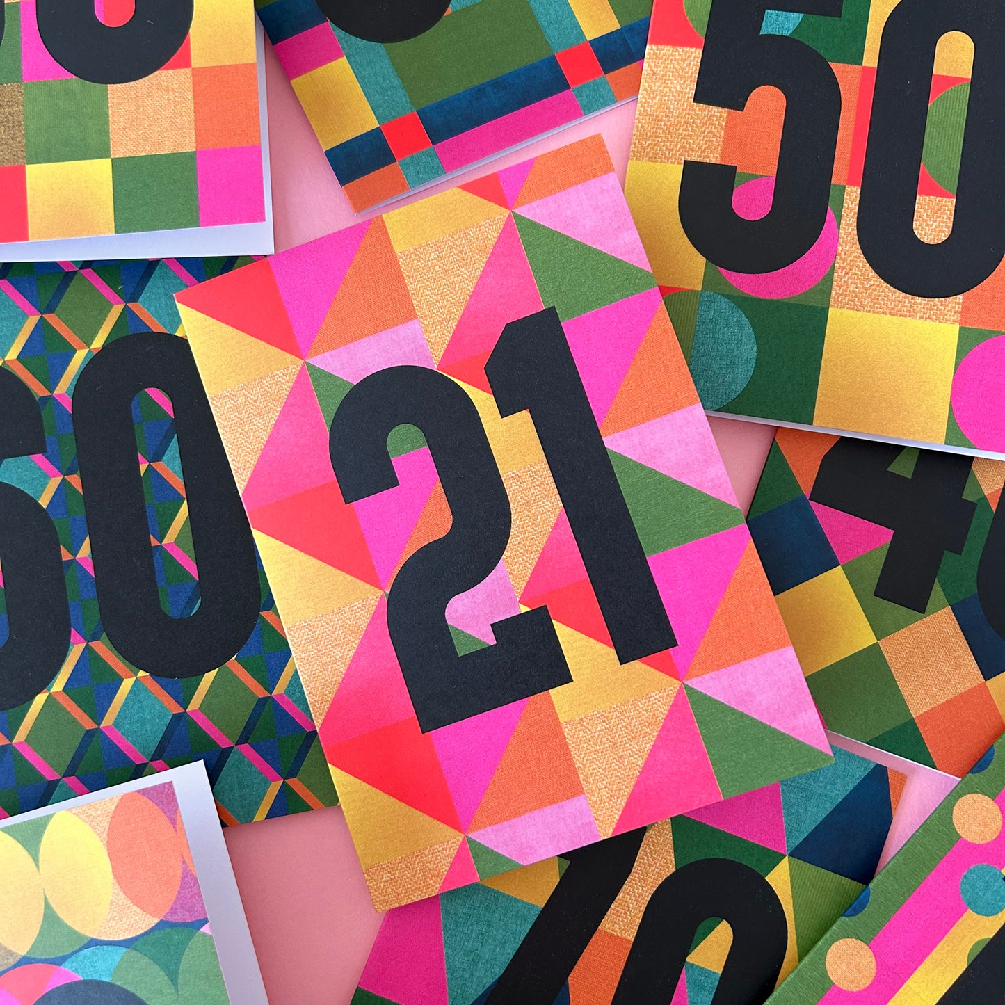 A close-up flat lay of colourful geometric cards or prints featuring large black numbers such as 21, 50, and 40 on bright pink, yellow, green, orange, and blue patterned backgrounds.