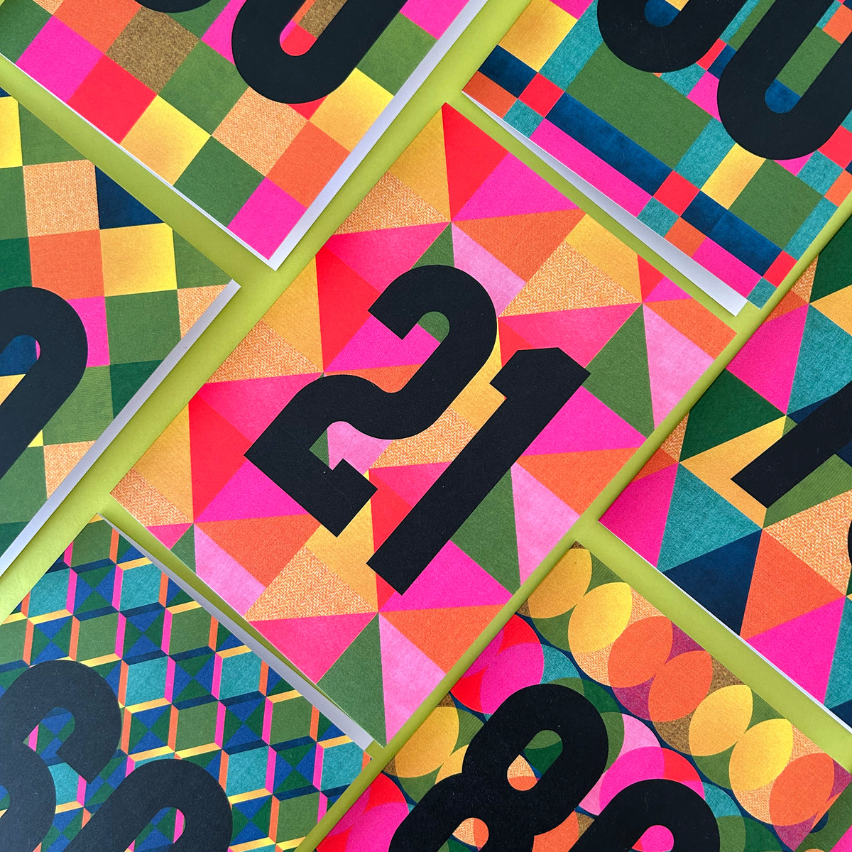 A close-up of a colourful geometric patterned card or print featuring large black numbers overlaid on bright pink, orange, green, yellow, and blue shapes.