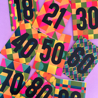 A flat-lay arrangement of colourful geometric cards featuring large black numbers from 18 to 90 on a solid purple background.