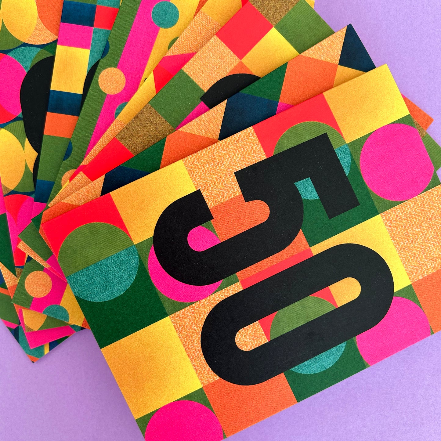 A stack of colourful patterned cards or envelopes fanned out on a lavender background. The top card features a bold black number 5 over a geometric patchwork design with yellow, orange, green, pink, and blue shapes.