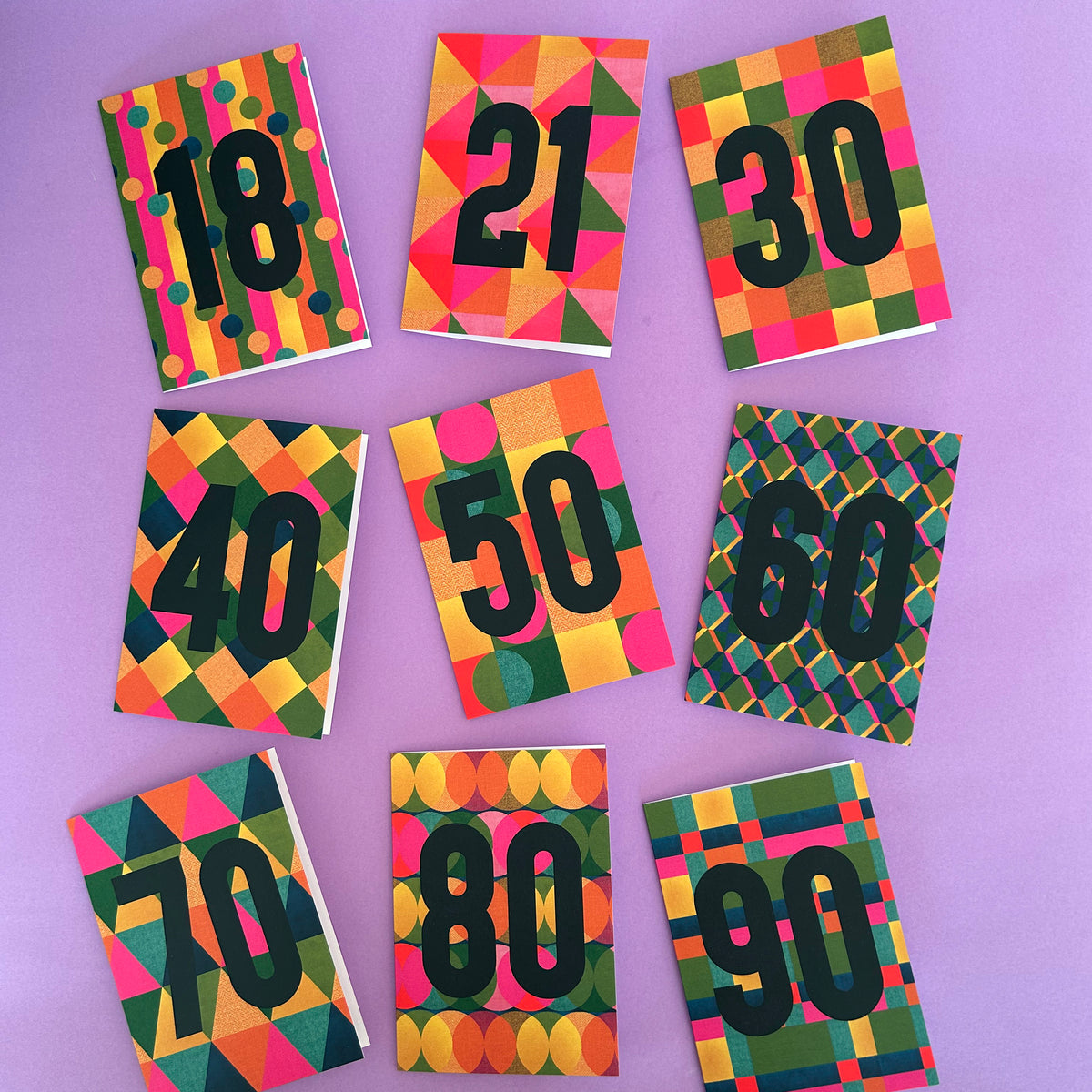 Nine colourful patterned cards arranged in a grid on a lavender background, each printed with a large black number from 18 to 90.