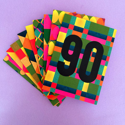 A stack of colourful patterned cards fanned out on a light purple background. The top card features a bold black '90' over a green, yellow, pink, and blue geometric plaid pattern.