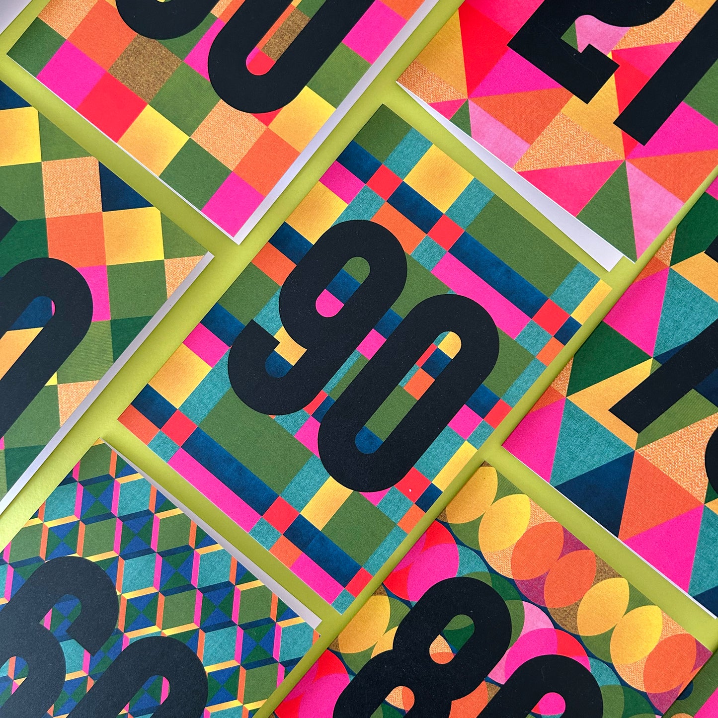 A close-up flat lay of several colourful patterned cards arranged diagonally. Each cover features bold black numbers over abstract geometric designs in pink, yellow, green, blue, orange, and purple.