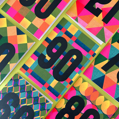 A close-up flat lay of several colourful patterned cards arranged diagonally. Each cover features bold black numbers over abstract geometric designs in pink, yellow, green, blue, orange, and purple.