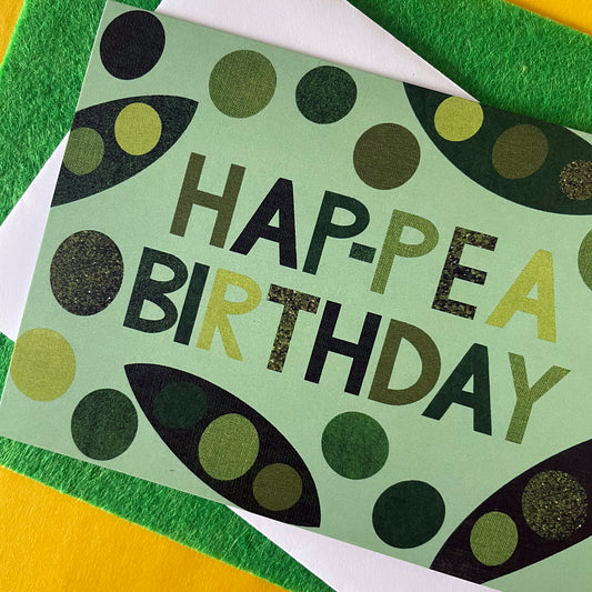 Close up Image of a light green card that says Hap-pea Birthday in bold lettering and has collaged illustrations of peas and pods