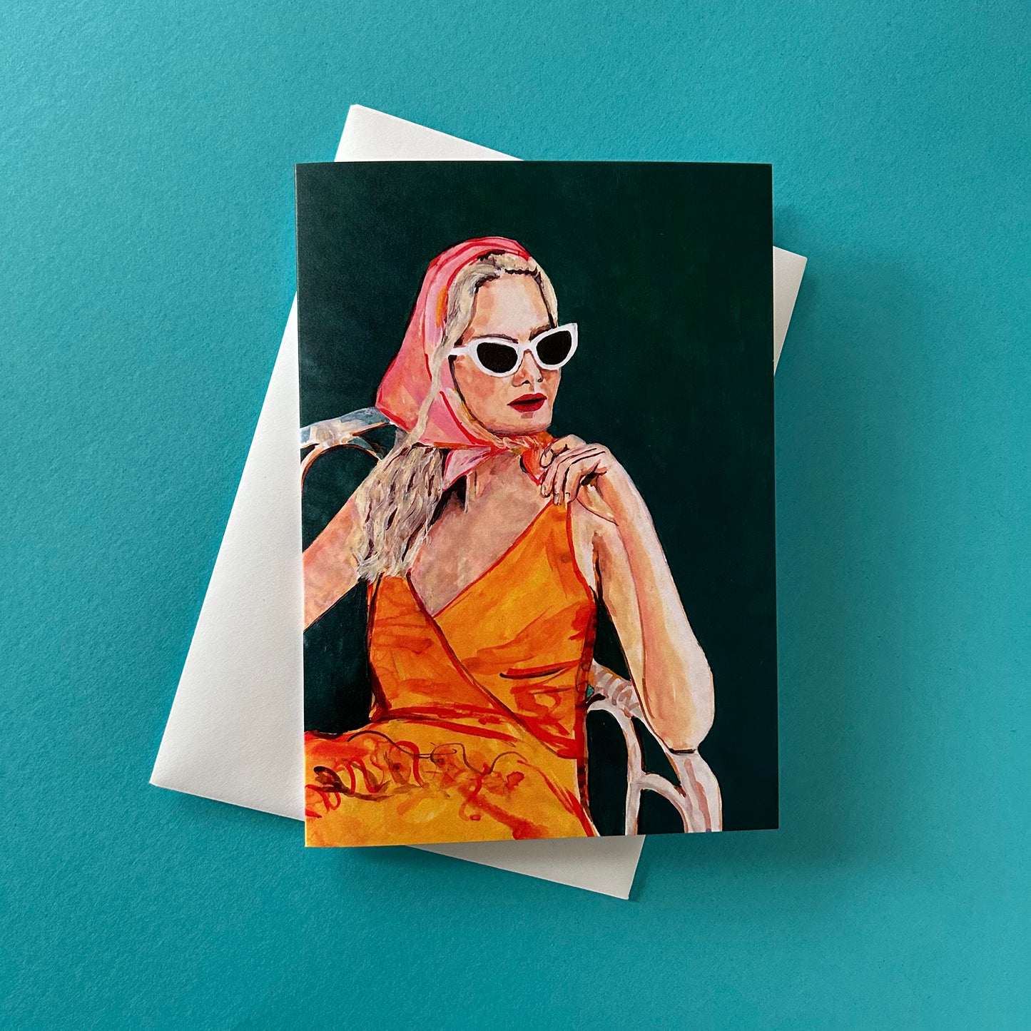 Greeting card with a painting of a woman in an orange dress and pink headscarf on a teal background.