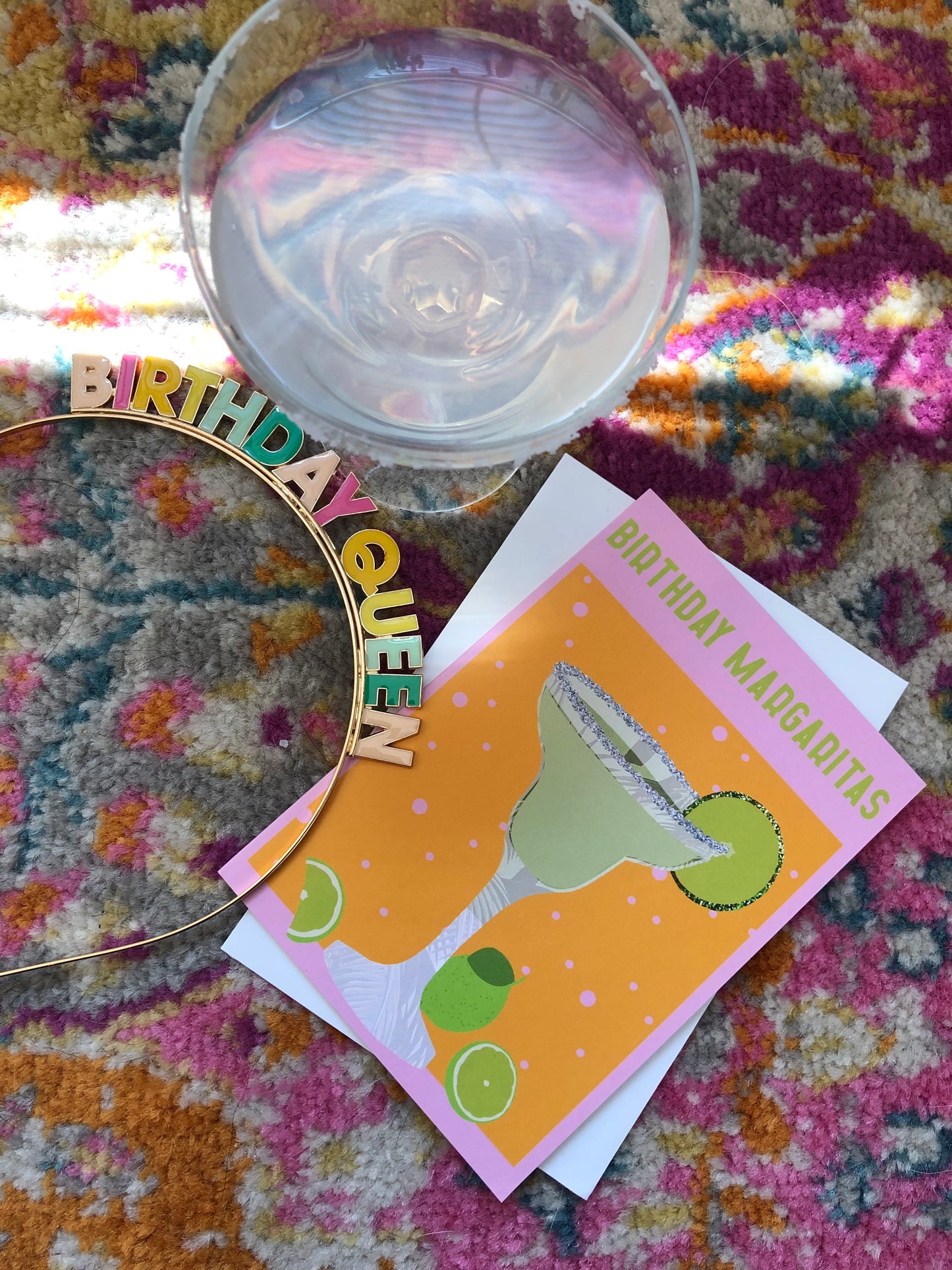 Bright and colourful birthday card featuring a margarita cocktail on a rug next to a glass and a birthday queen headband.