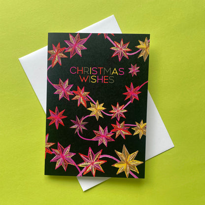 A Christmas greeting card with a black background and colourful star designs, placed on top of a white envelope against a bright lime green background.
