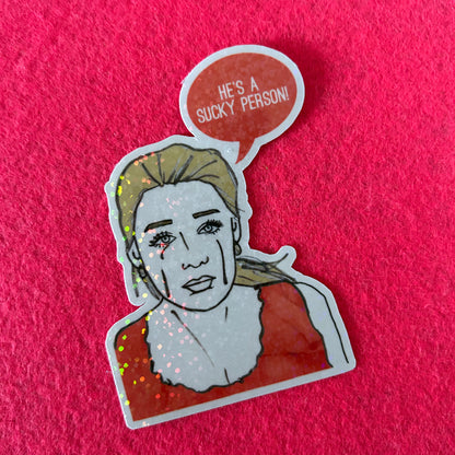 Sticker of a person with a speech bubble saying 'He's a sucky person!' on a pink background