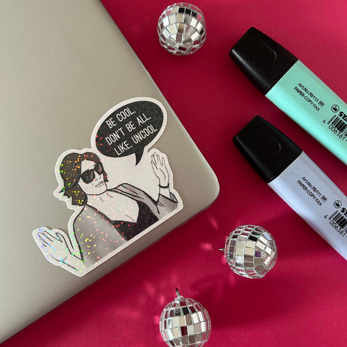 Sticker with a woman and speech bubble on a reflective surface with disco balls and markers.