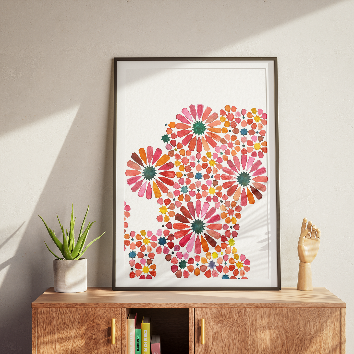 Framed floral artwork on a wall above a wooden cabinet with a plant and books.
