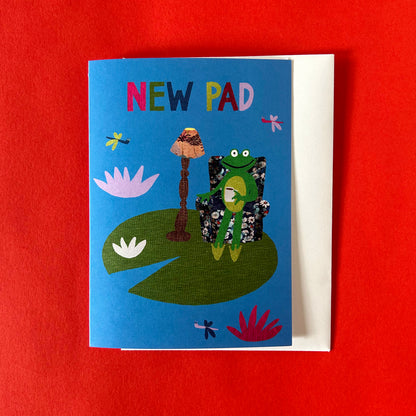 Greetings card with a frog illustration on a blue background, sitting on a red surface.
