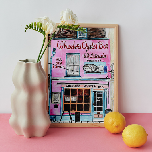 Framed artwork of Wheelers Oyster Bar with a vase and lemons on a pink surface.