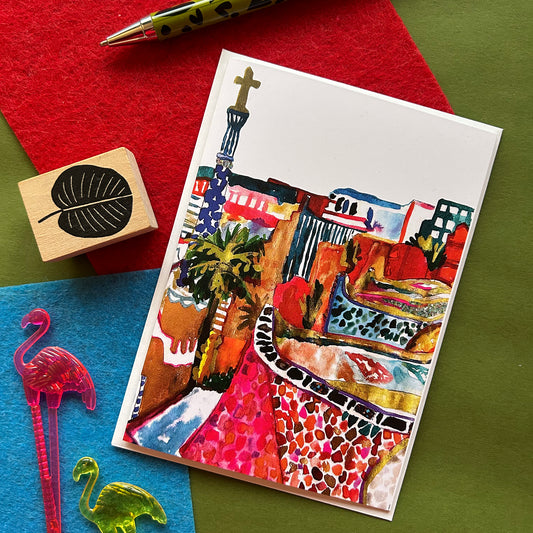 Colourful greeting card with artistic design of Parc Guell in Barcelona, on a green surface with stationery items.